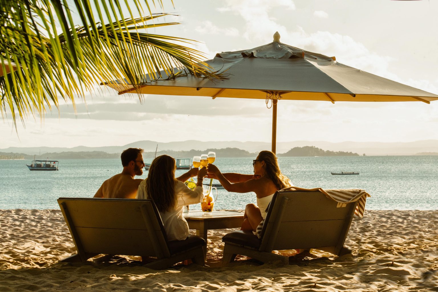 Quatro pessoas brindando à mesa na areia, de frente para o mar, no fim de tarde no Obar, em Barra Grande — Península de Maraú