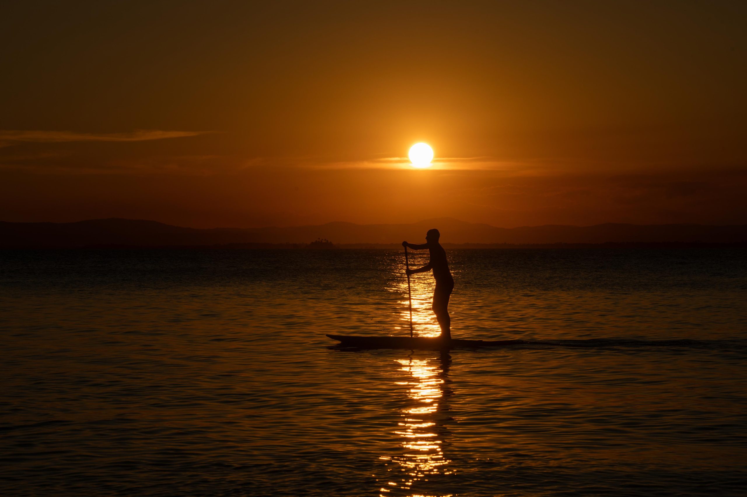 Praticante de stand up paddle em silhueta contra o sol poente, na Baía de Camamu
