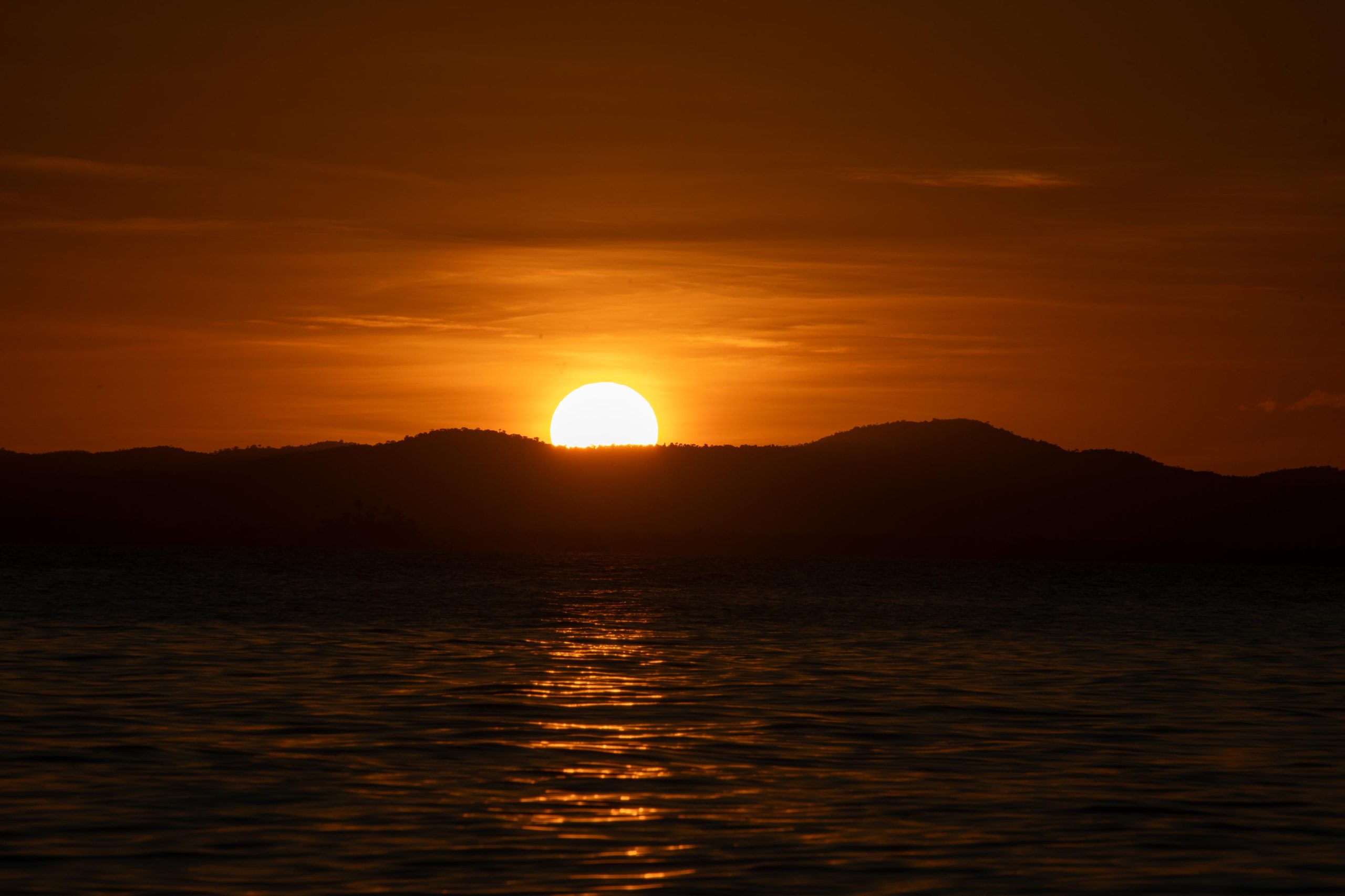 O sol se pondo atrás das colinas do continente, visto da Ponta do Mutá, em Barra Grande