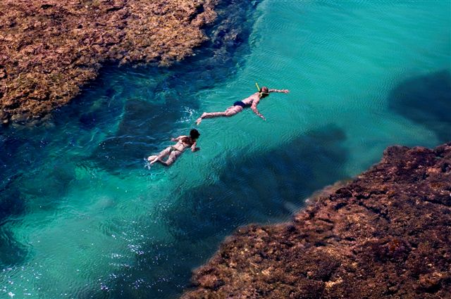 Duas pessoas nadando de snorkel na água transparente de uma piscina natural de Taipu de Fora