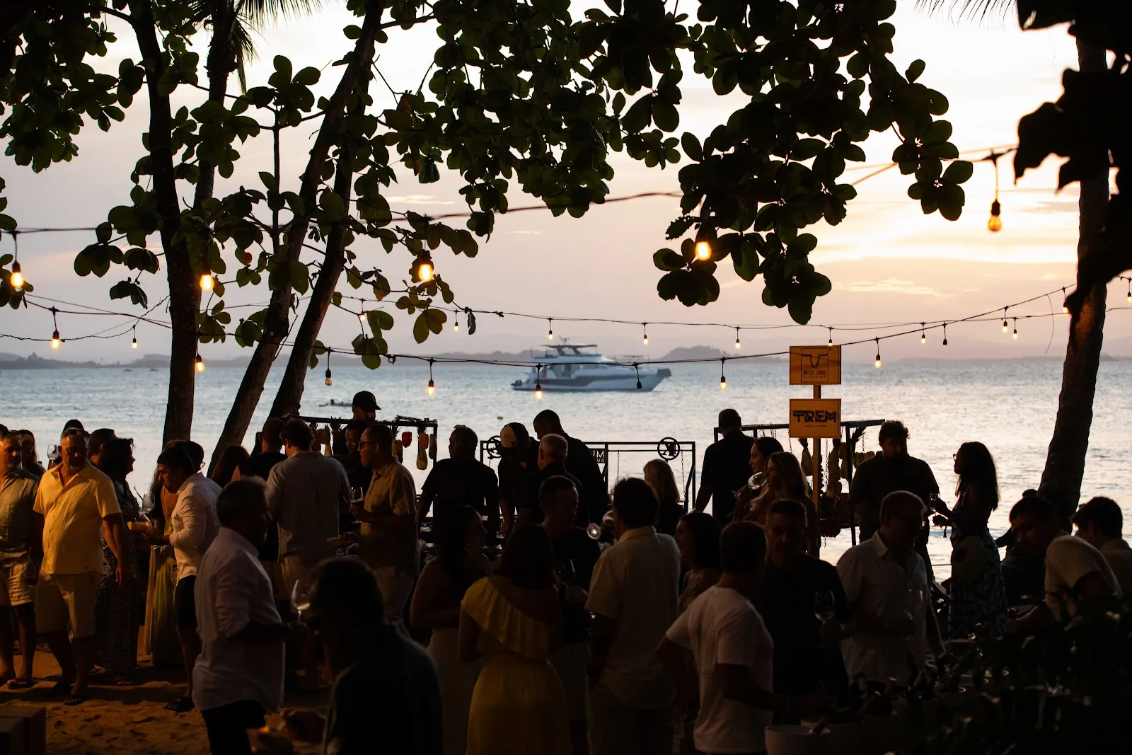 Casa cheia sob as árvores e os varais de luz, virada para o mar no pôr do sol do Wine Festival Obar 2026