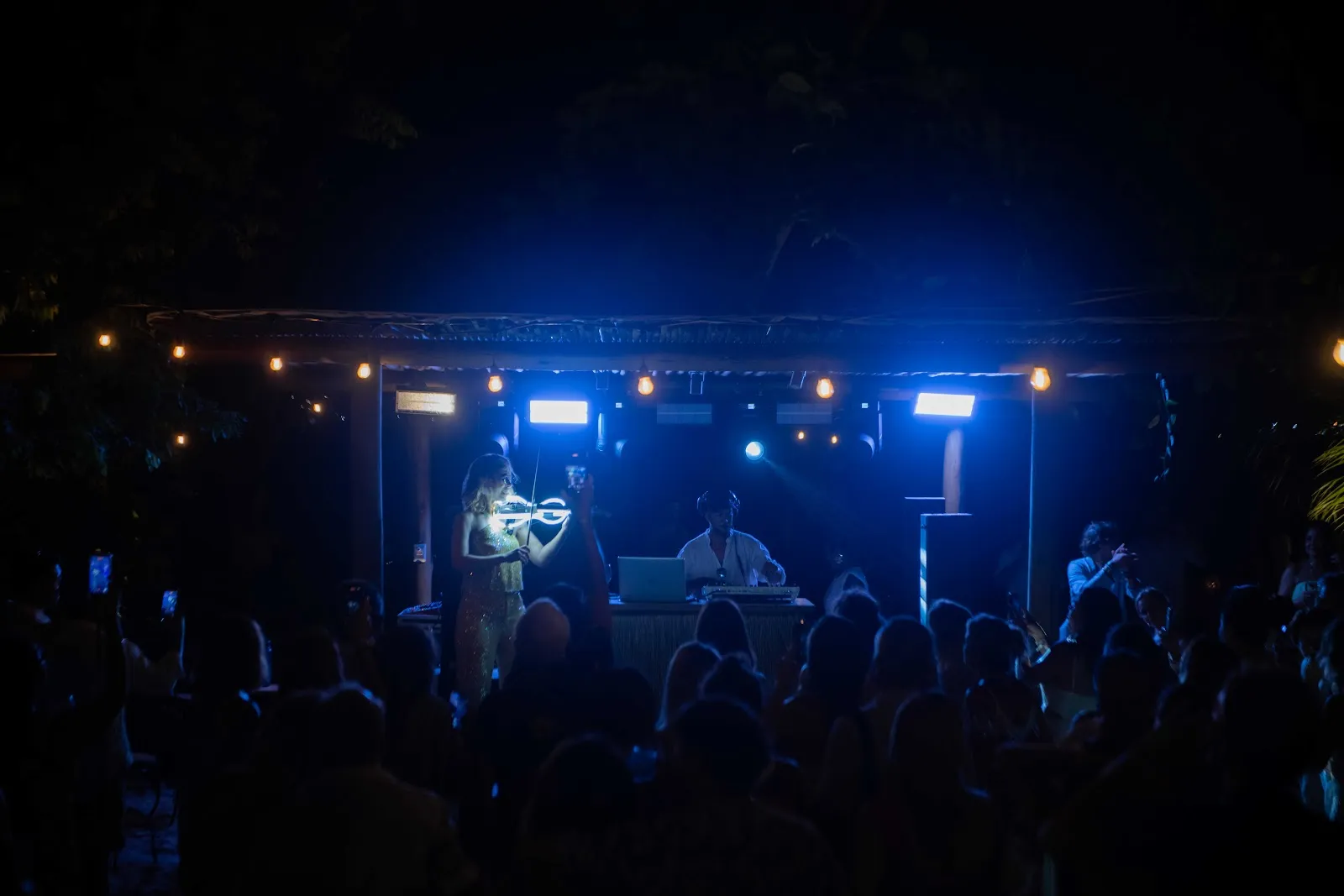 DJ Joel e a violinista Karen Machado no palco, sob luz azul, com a pista cheia à frente