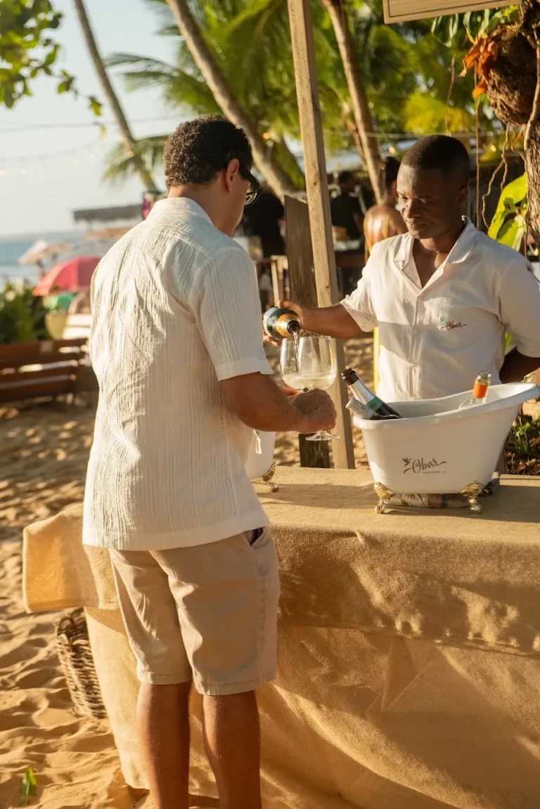 Atendente servindo vinho no estande, na areia, com o sol da tarde